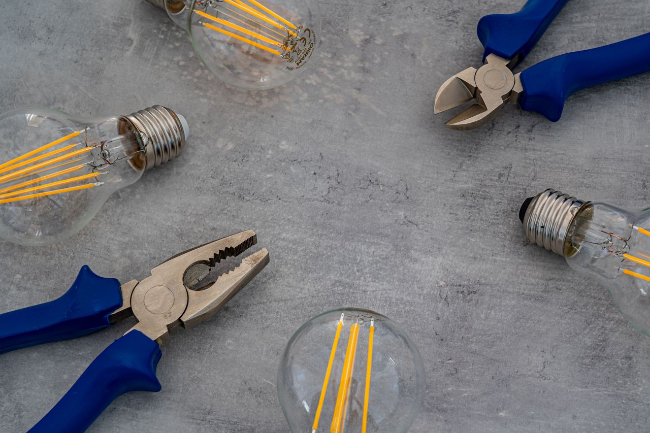 A flat lay of vintage Edison bulbs and pliers on a gray surface, emphasizing industrial design.